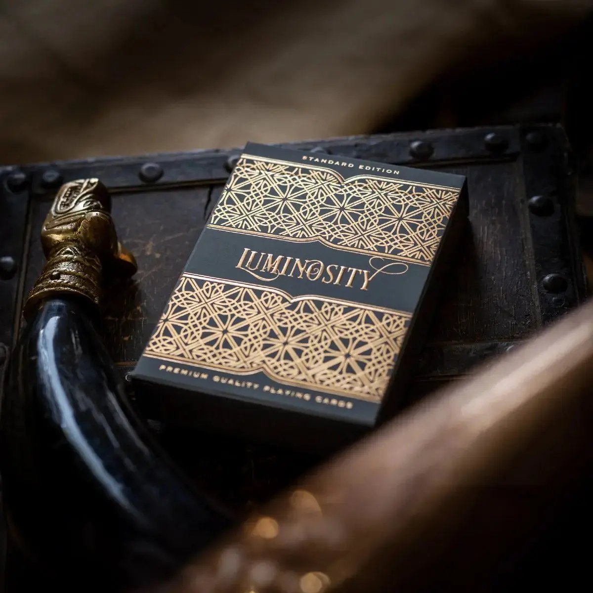 Luminosity playing cards in a black box with intricate gold designs on a wooden surface